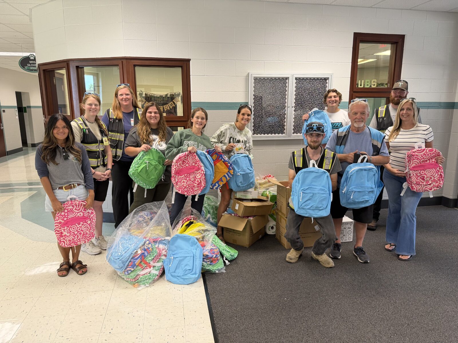TALA Logistics team members and school staff holding donated backpacks and school supplies in a school hallway.