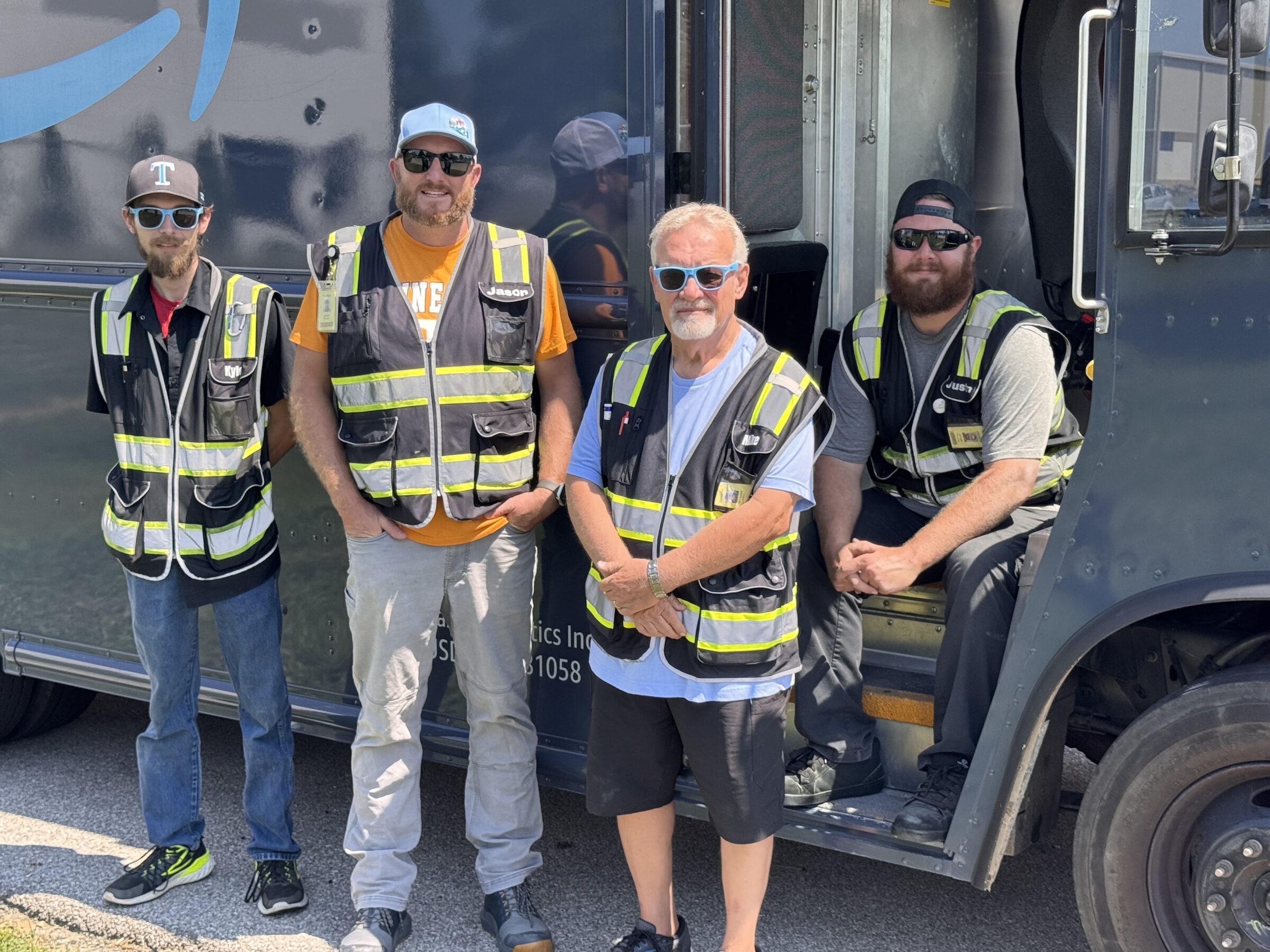 Four TALA Logistics delivery associates in high-visibility safety vests beside an Amazon delivery truck.